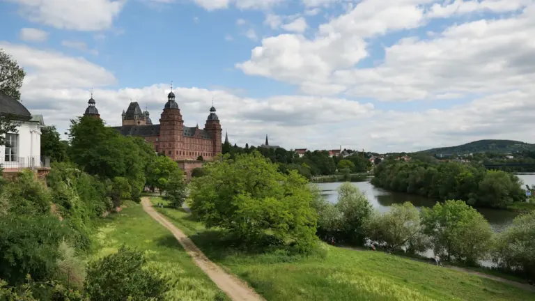 Schloss Johannisburg am Mainufer bei Aschaffenburg unter blauem Himmel mit grünen Bäumen.