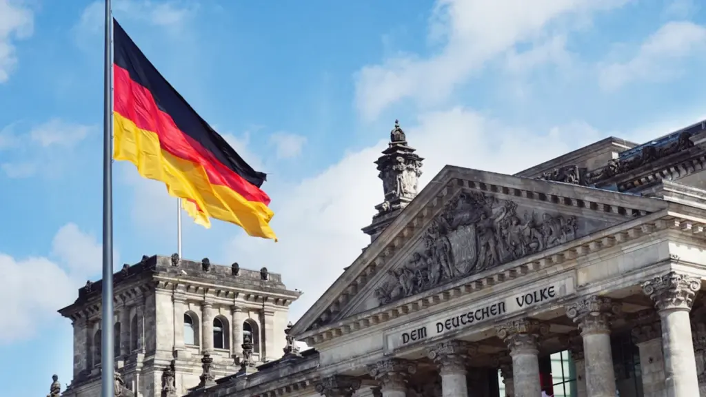 Die deutsche Flagge weht vor dem Reichstagsgebäude in Berlin bei blauem Himmel.