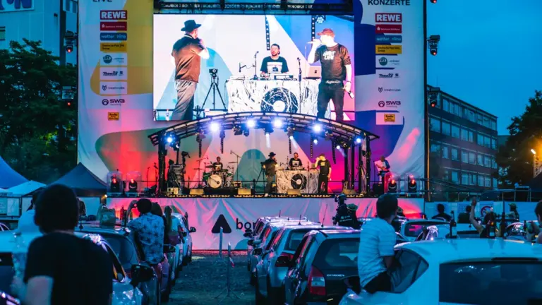 Live-Konzert auf einer großen Bühne vor parkenden Autos in der Stadt Bonn am Abend.