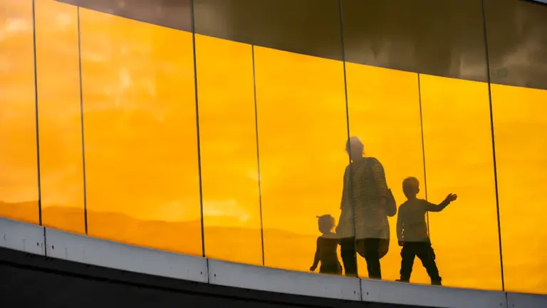 Silhouetten von Menschen vor einer leuchtend orangen Glasfassade in einem Museum.