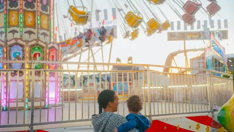 Mutter und Kind vor einem bunten Kettenkarussell auf einem Jahrmarkt bei Sonnenuntergang.