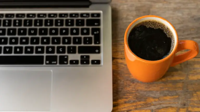 Ein Laptop und eine Tasse Kaffee auf einem hölzernen Schreibtisch im Büro.