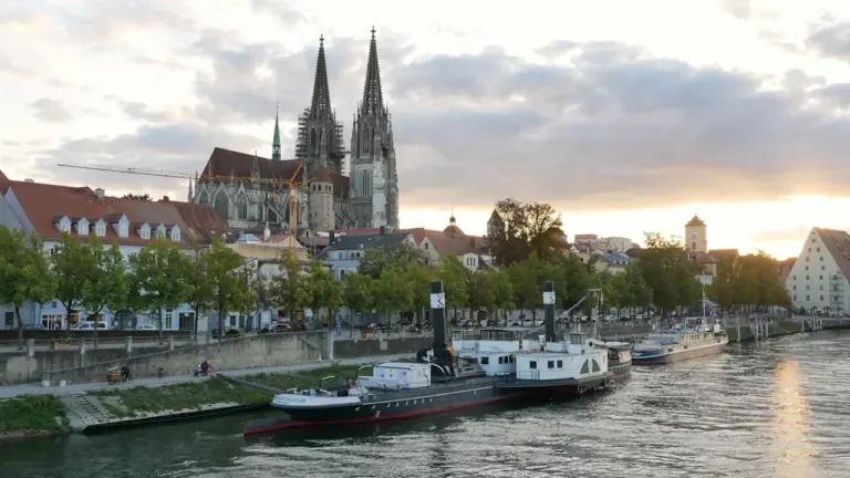 Blick auf den Regensburger Dom und historische Schiffe am Ufer der Donau.