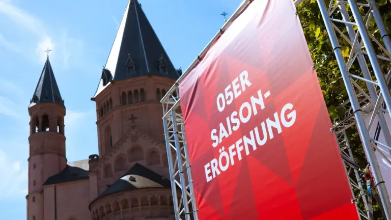 Rotes Banner vor einer historischen Kirche in Deutschland bei strahlend blauem Himmel.
