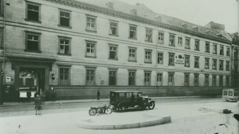 Historisches Gebäude des Polizeipräsidiums mit einem davor parkenden alten Auto und einem Motorrad.