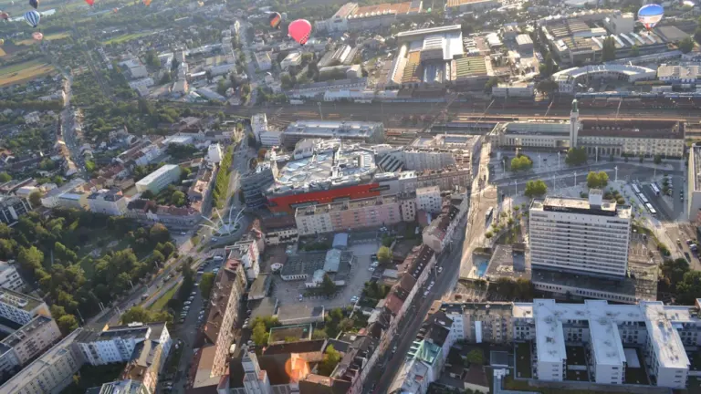 Bunte Heißluftballons über einer städtischen Szenerie bei Sonnenaufgang am frühen Morgen.