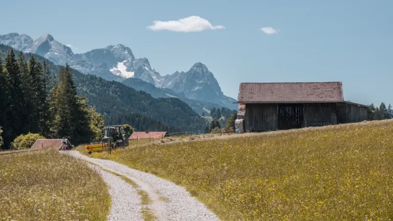 Ein idyllischer Feldweg führt an einer historischen Scheune vorbei in eine deutsche Hügellandschaft.