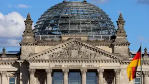Das Reichstagsgebäude mit der gläsernen Kuppel und wehender deutscher Flagge bei Sonnenschein.
