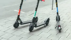 Drei E-Scooter stehen ordentlich nebeneinander auf einem gepflasterten Gehweg in einer Stadt.