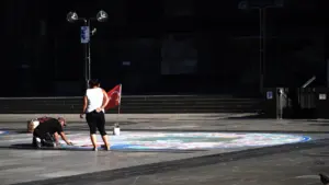 Personen gestalten gemeinsam mit bunter Kreide ein Bodenbild auf einem öffentlichen Stadtplatz.