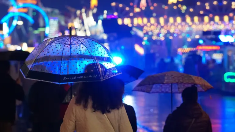 Menschen mit Regenschirmen bei Nacht auf einem beleuchteten Jahrmarkt in München.