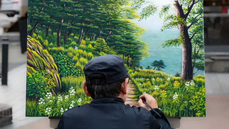 Ein Künstler malt eine detailreiche Waldlandschaft auf einer Leinwand im Freien.