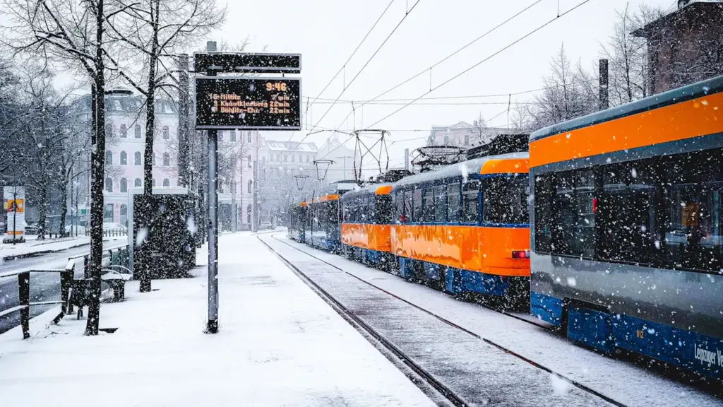 Orangefarbene Straßenbahn an einem deutschen Bahnhof während eines winterlichen Schneefalls.